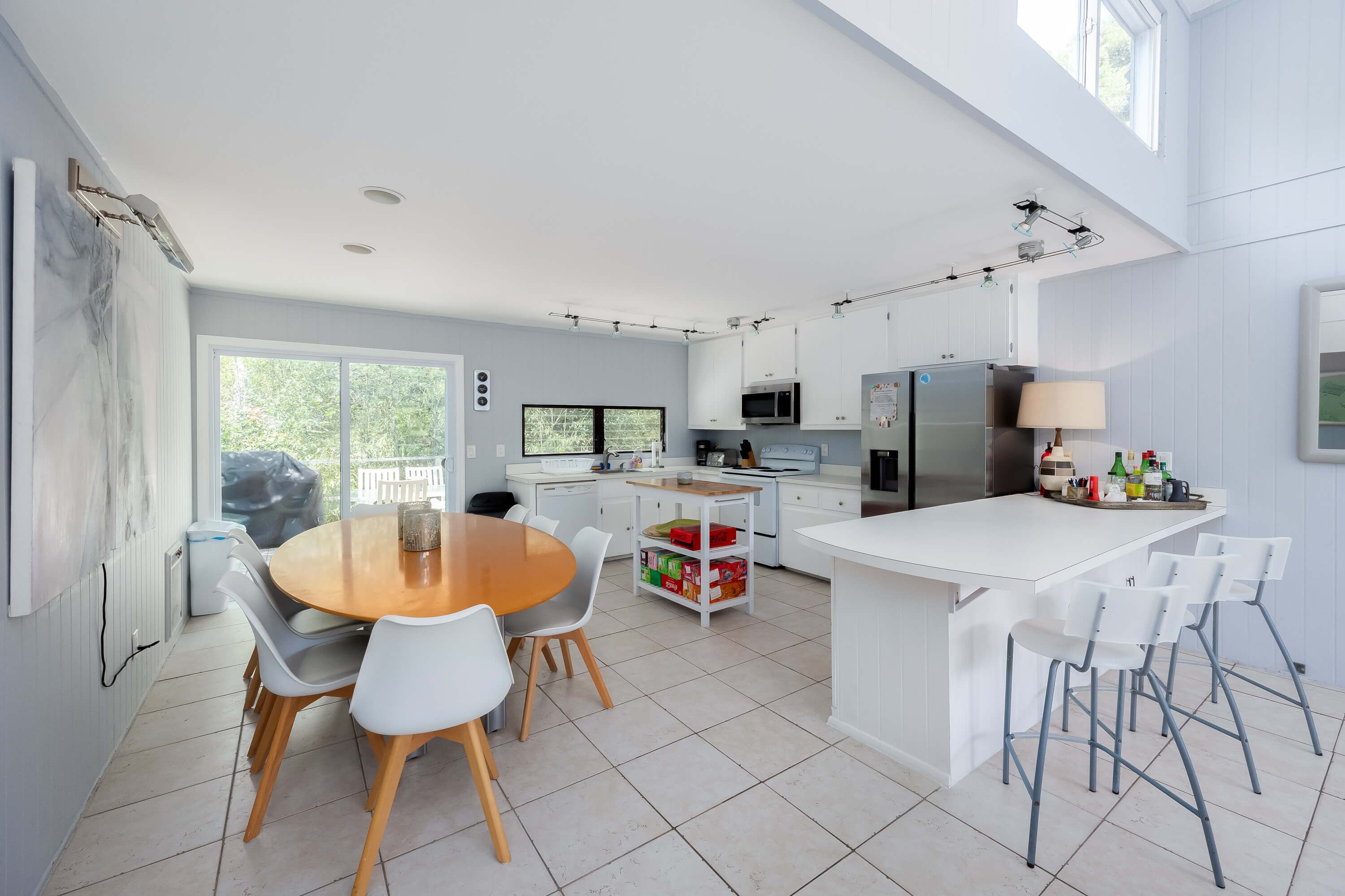 A modern kitchen with white cabinetry, a central island with bar stools, and a dining area with a round table and chairs.