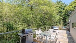 Una terraza con parrilla, mesa y sillas al aire libre, rodeada de abundante vegetación.