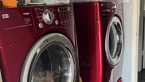 Two red front-loading washing machines in a laundry room with a wooden floor.