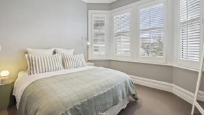 A bedroom with a bed, nightstands, and a window with blinds. - Villa on Rattray (Dunedin)