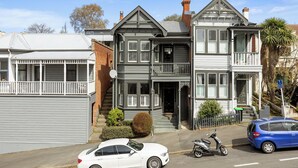 A Victorian-style house with a balcony, a garage, and a driveway with parked cars. - Villa on Rattray (Dunedin)