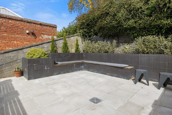 Une terrasse sur le toit équipée d’un banc intégré, de plantes en pot et d’une grille de protection pour l’évacuation de l’eau.
