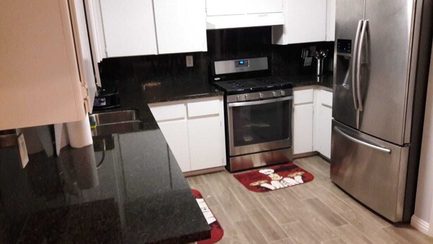 Una cocina moderna con armarios blancos, encimera negra, electrodomésticos de acero inoxidable y una alfombra roja.