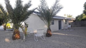 Una casa con entrada de grava, dos sillas de metal blanco y dos palmeras.