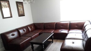 Un salón con muebles de esquina, un sofá seccional de cuero marrón, una mesa de centro de madera oscura y una araña.