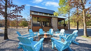 Una cabaña con fachada de piedra, un porche cubierto y un brasero con sillas Adirondack.