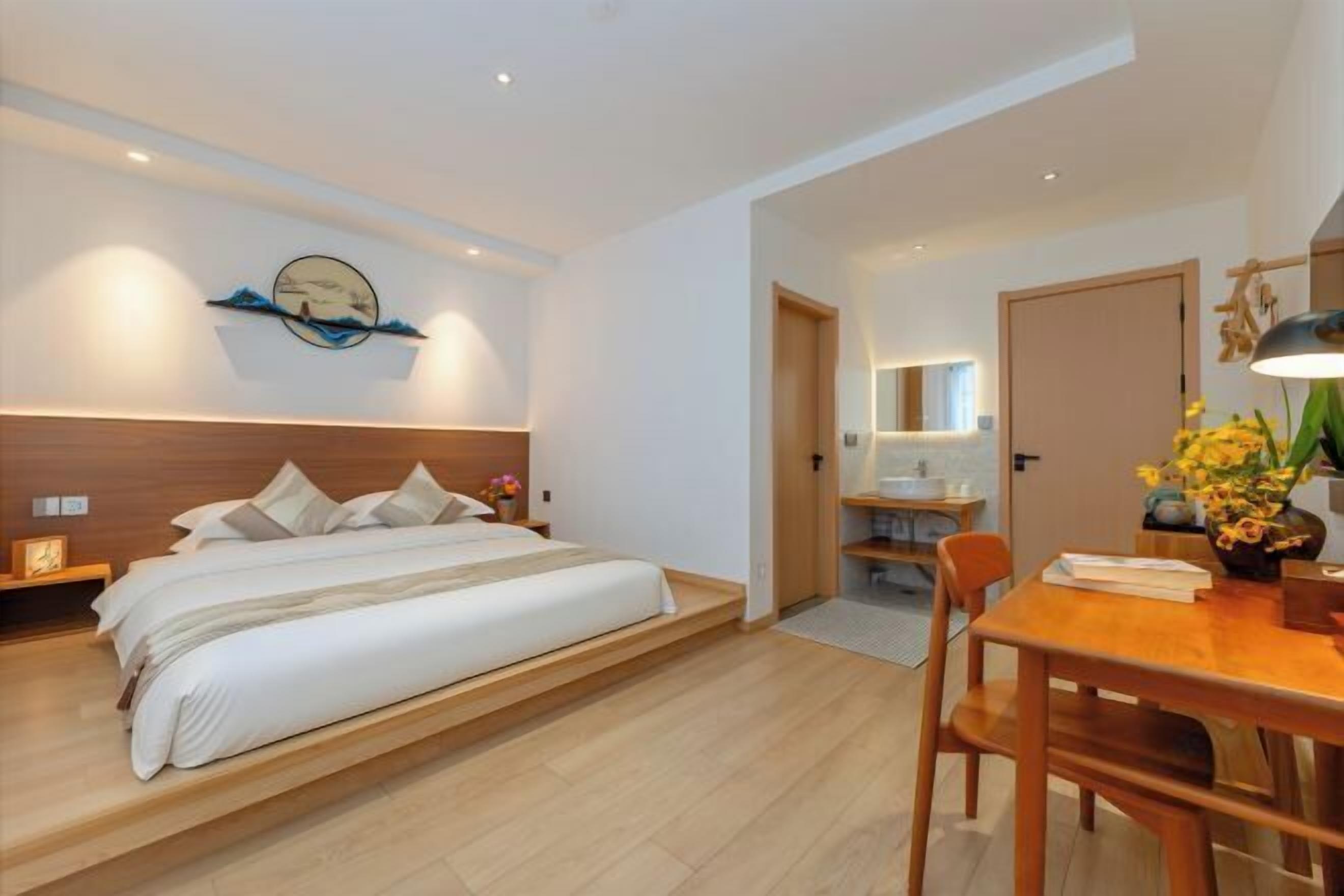 A bedroom with a bed, bedside tables, a desk with a chair, and a bathroom visible in the background.
