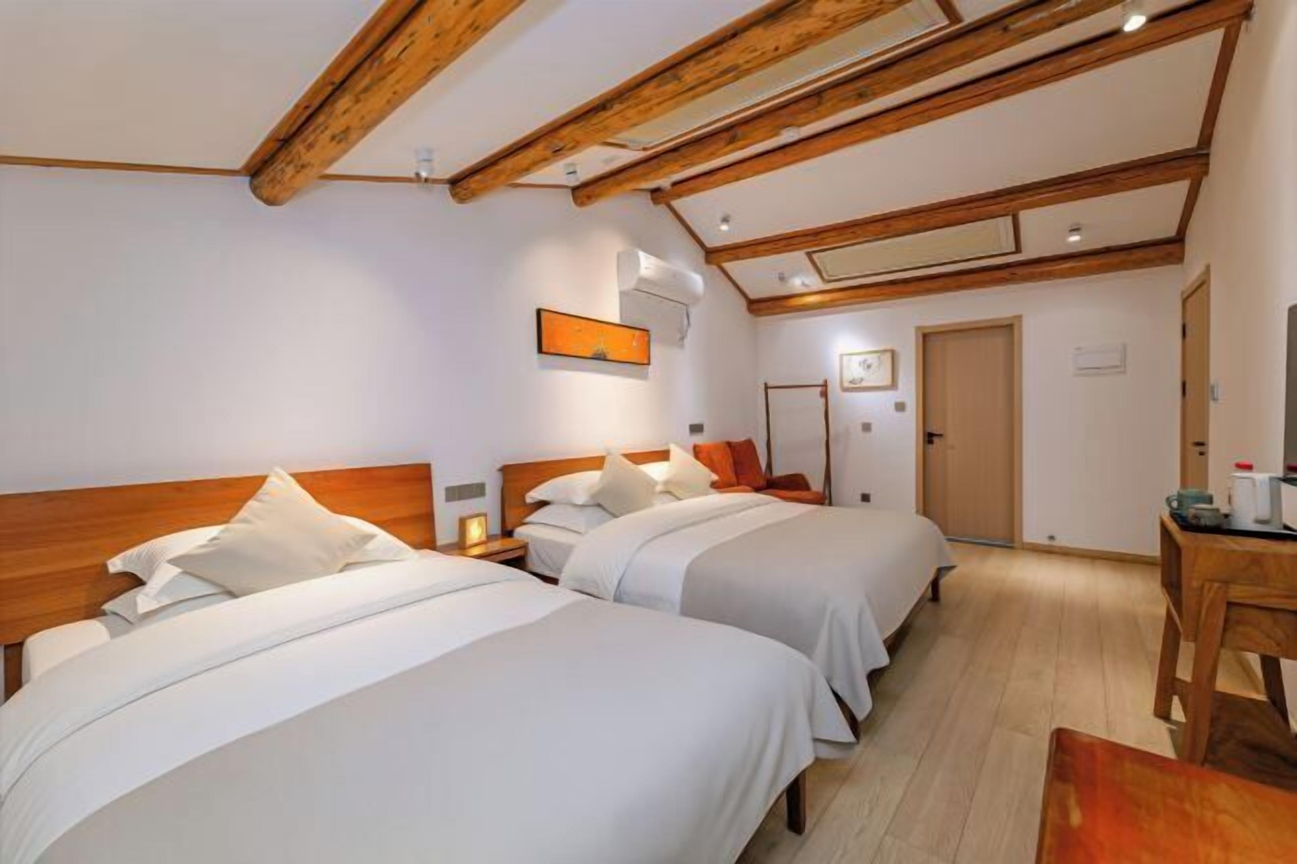A hotel room with two beds, wooden beams, a desk, and a chair.