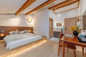 Un dormitorio con cabecera de madera, cama con almohadas, mesita de noche, escritorio con silla y espejo.