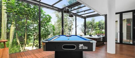A pool table in a room with large windows, wooden flooring, and a modern design.