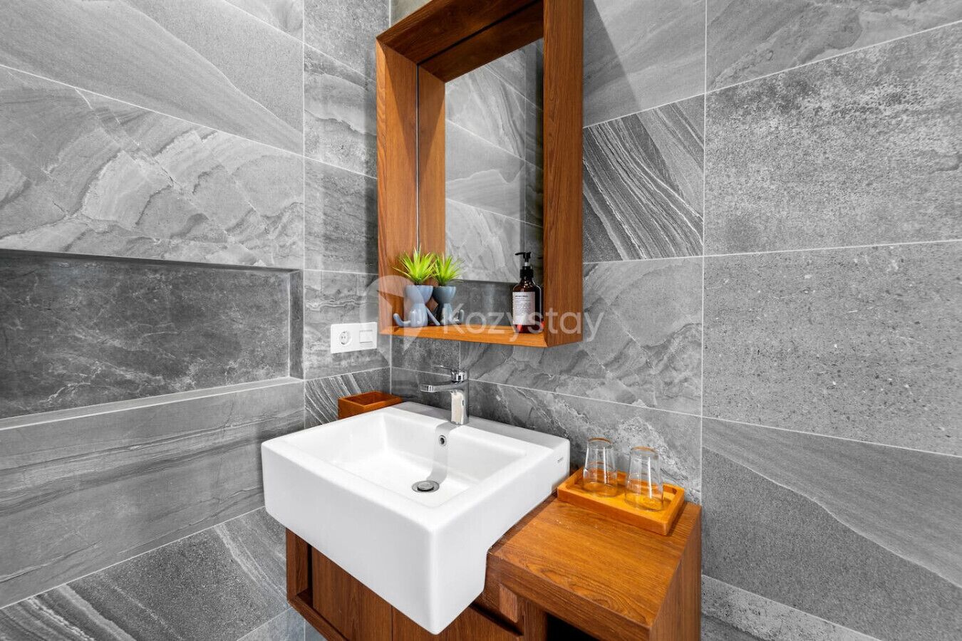 A modern bathroom with a white sink, wooden vanity, and a mirror above.