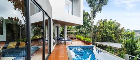 A modern house with a glass facade, a wooden deck, and a swimming pool.