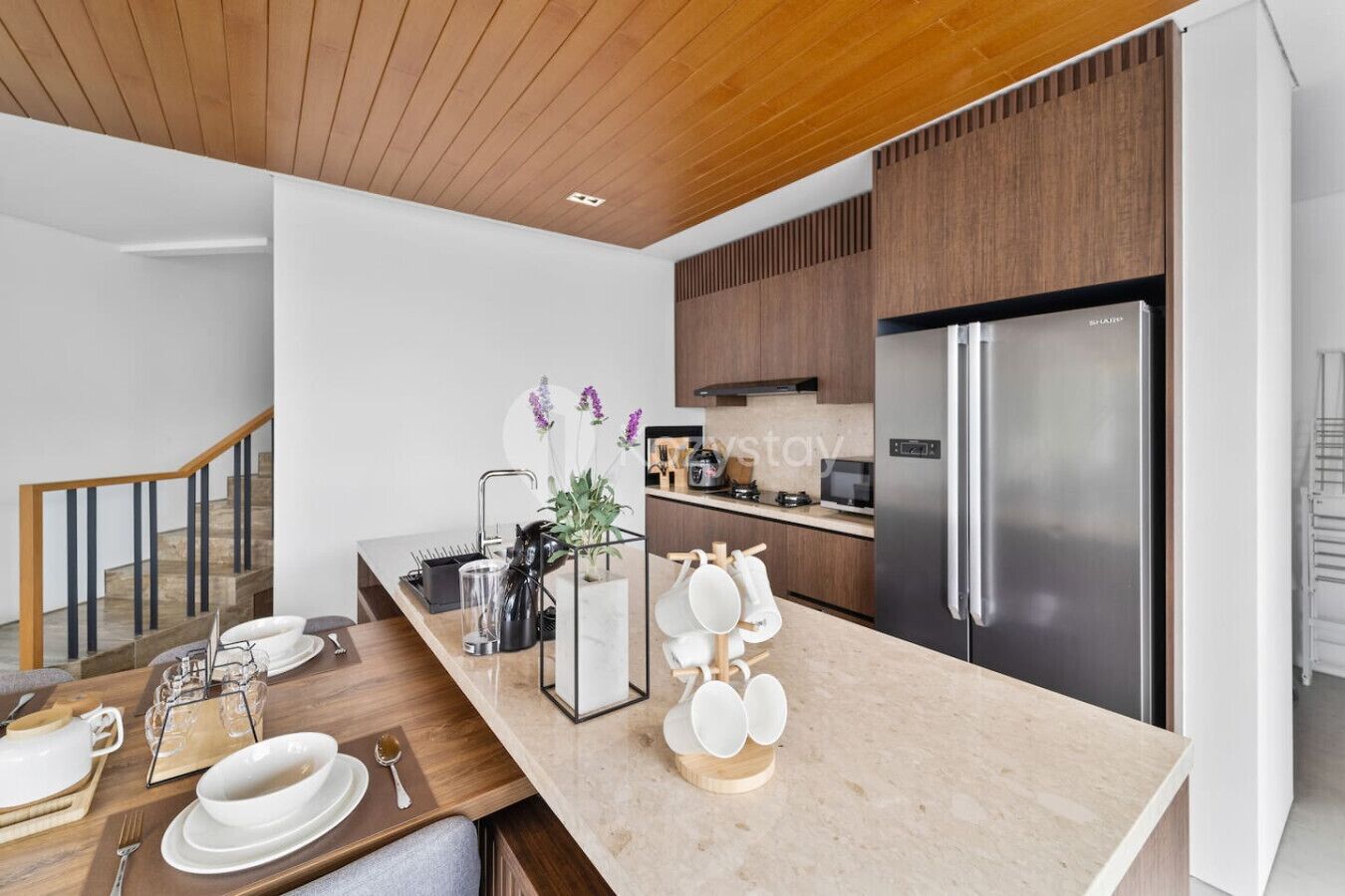 A modern kitchen with a stainless steel refrigerator, wooden cabinets, and a marble countertop.