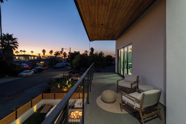 A balcony with a fire pit, seating, and a view of the street at dusk.