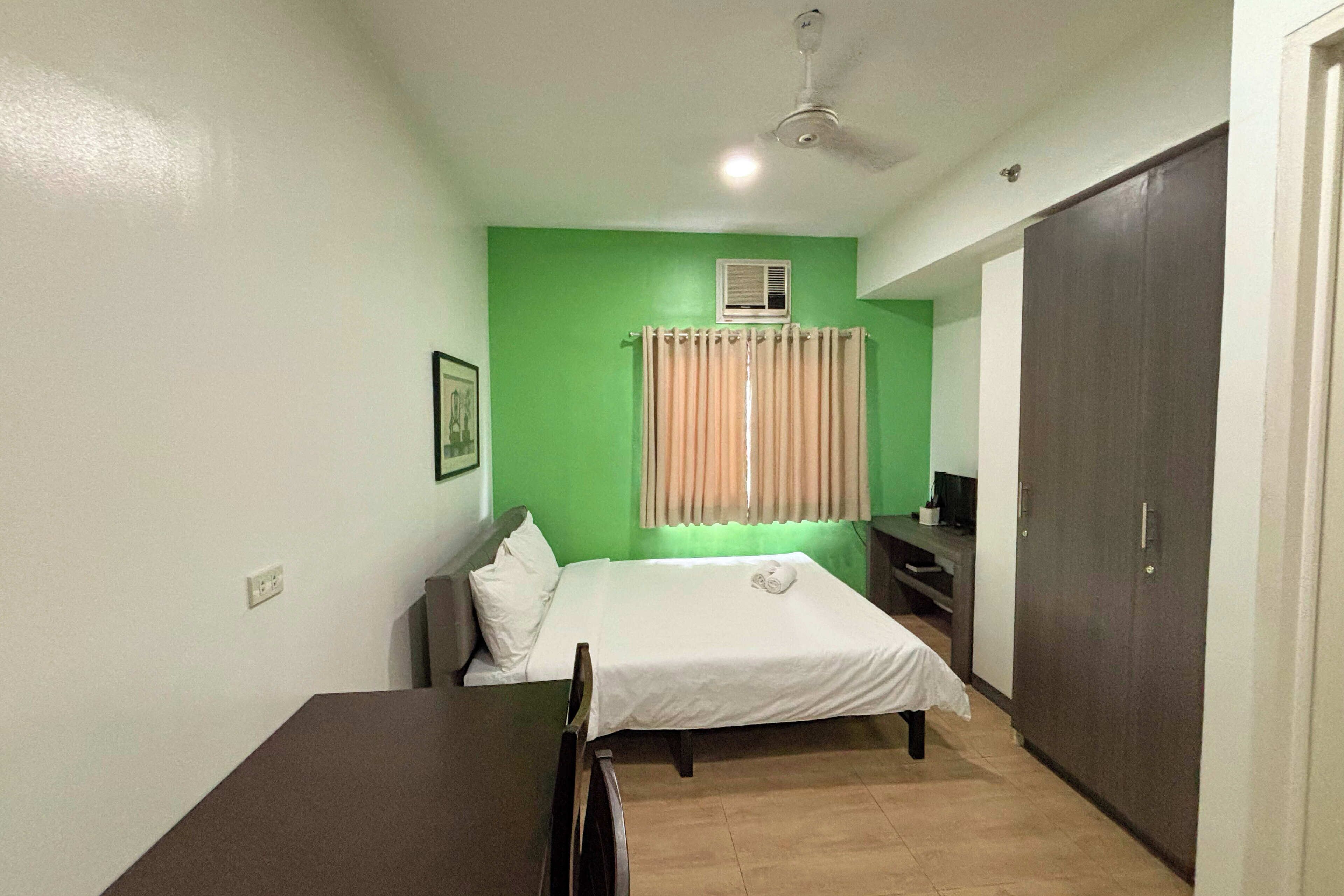 A room with a bed, a desk, a chair, a wardrobe, and a ceiling fan.