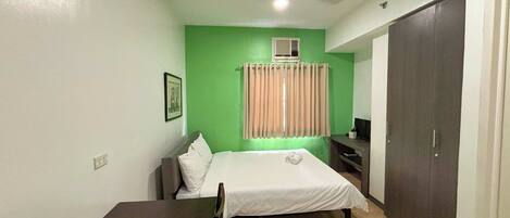 A room with a bed, a desk, a chair, a wardrobe, and a ceiling fan.