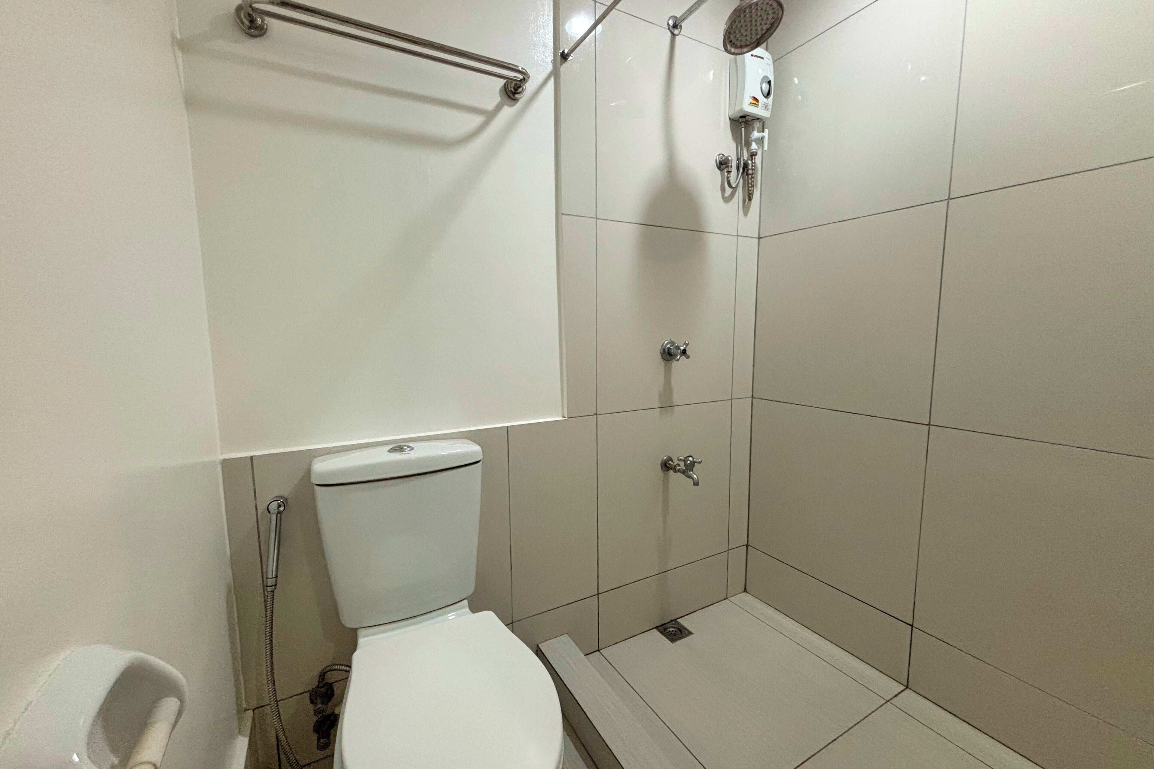 A small, modern bathroom with a toilet, a shower, and a handrail.
