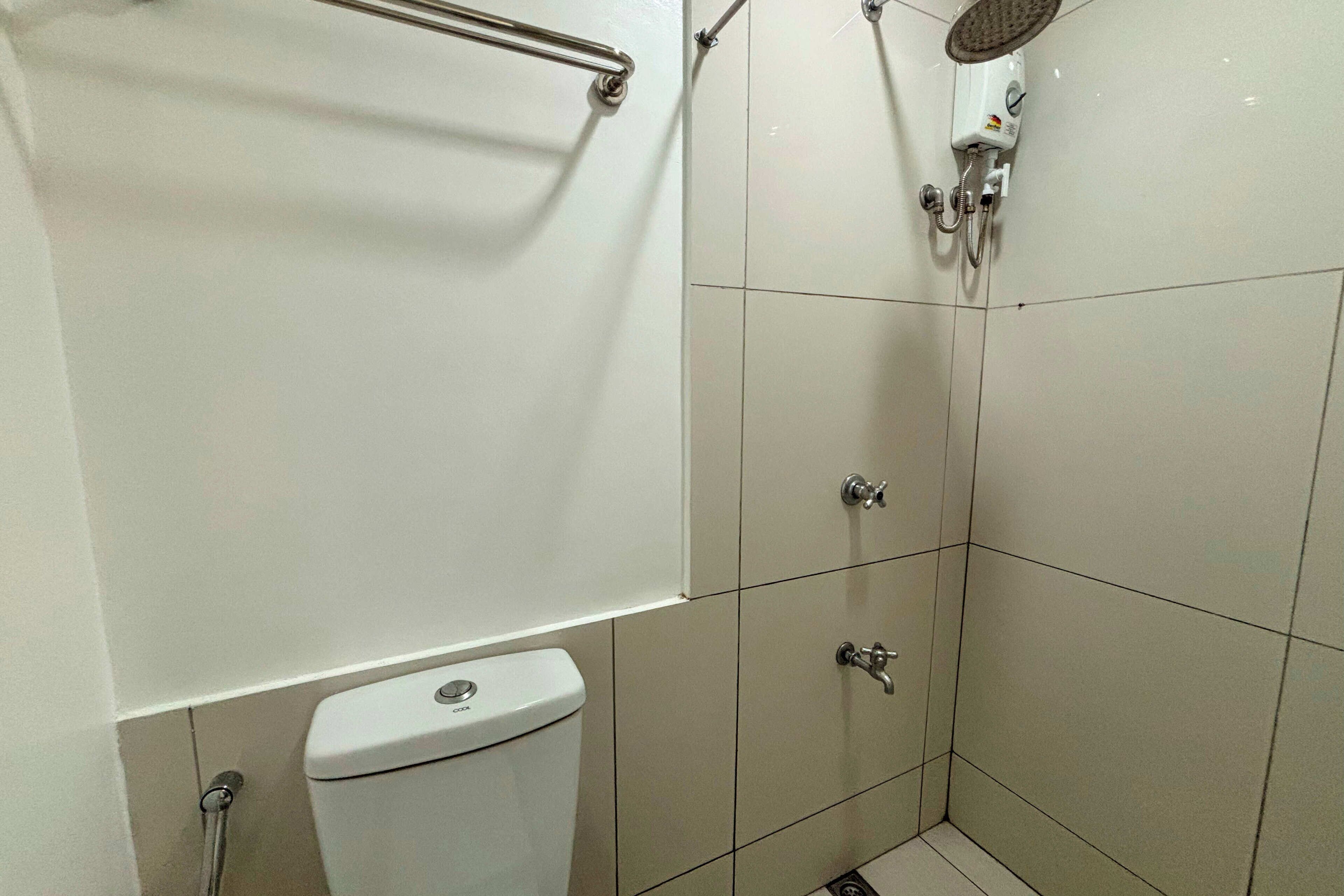 A small, clean bathroom with a toilet, a shower, and a handrail.