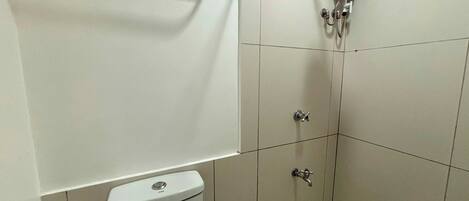 A small, clean bathroom with a toilet, a shower, and a handrail.