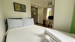 A hotel room with a bed, a desk, a chair, a painting, and a window with curtains. - Casa Lily Hotel Quezon City (Quezon City)