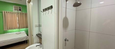 Une salle de bain avec une douche, un lavabo et un lit dans la pièce adjacente.