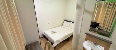 A small, clean room with a bed, a desk, a chair, a sink, and a ceiling fan.