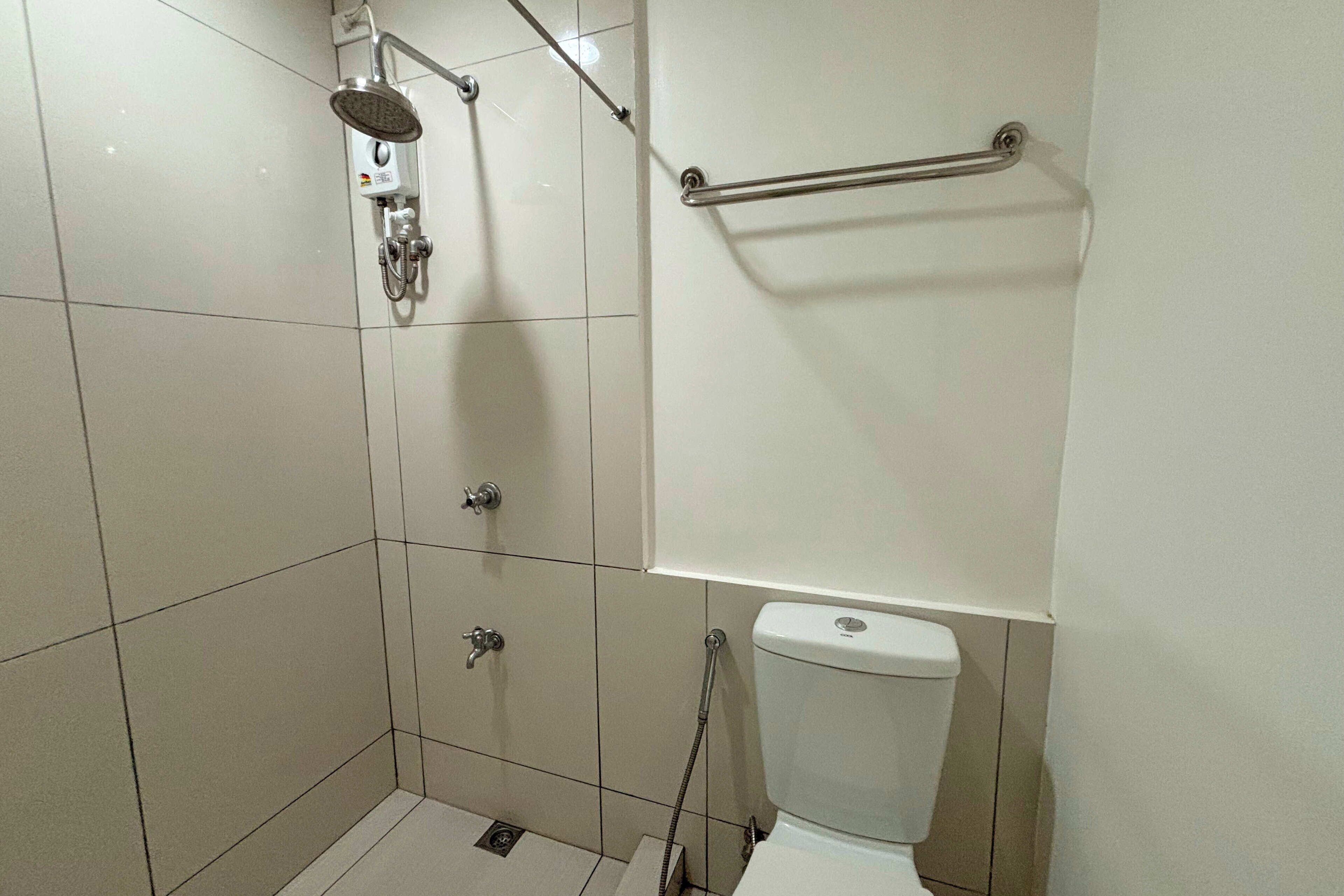 Un baño pequeño con azulejos, ducha, inodoro y una barra de apoyo.
