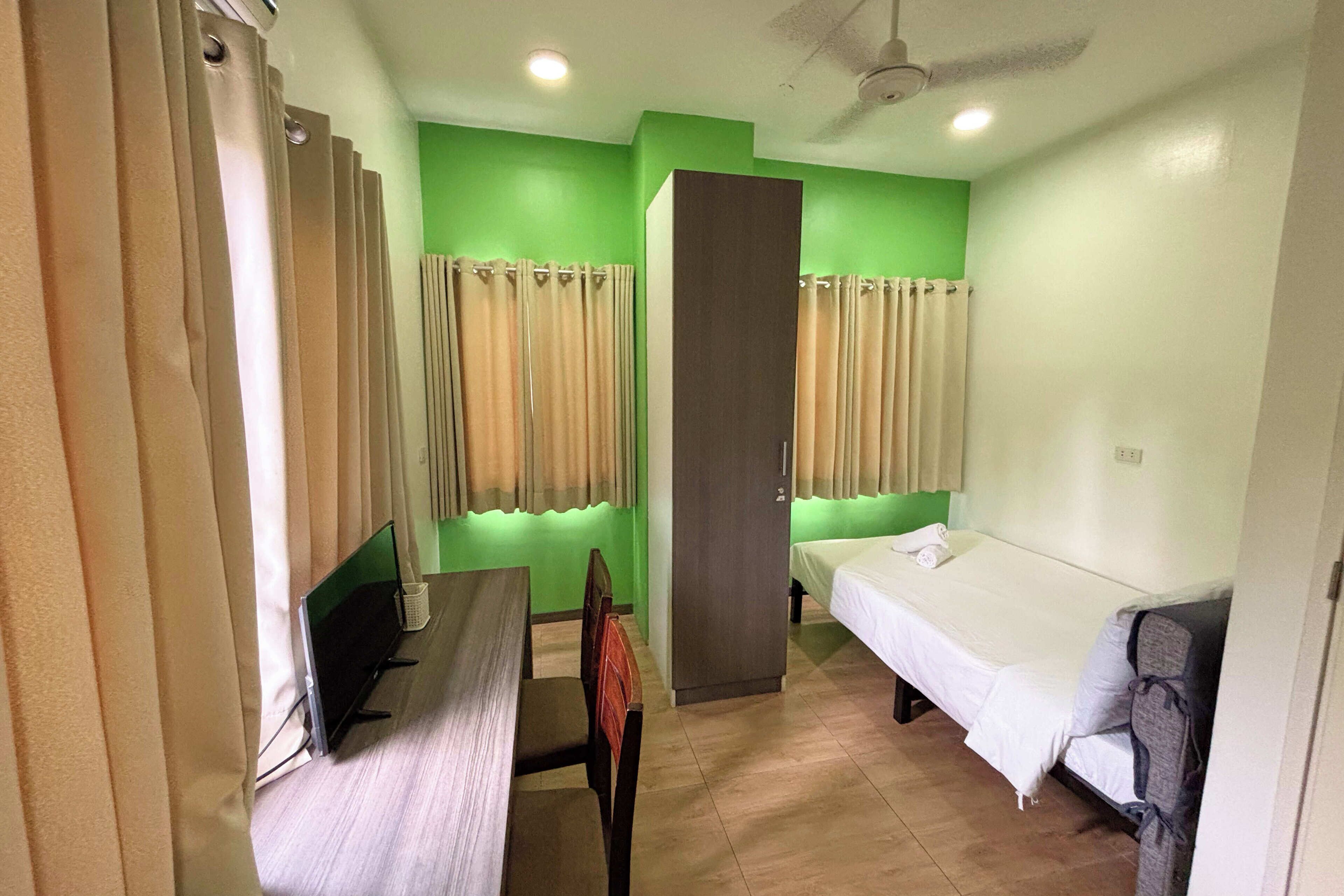 A hotel room with a bed, a desk with a computer, a chair, and a wardrobe.