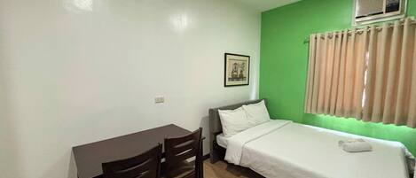 A small, clean room with a bed, a desk, and two chairs.