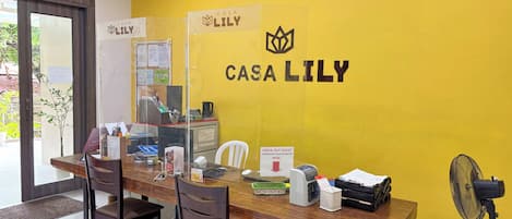 Een receptiegedeelte met een houten bureau, stoelen, een receptiebalie en een muur met het logo 'Casa Lily'.