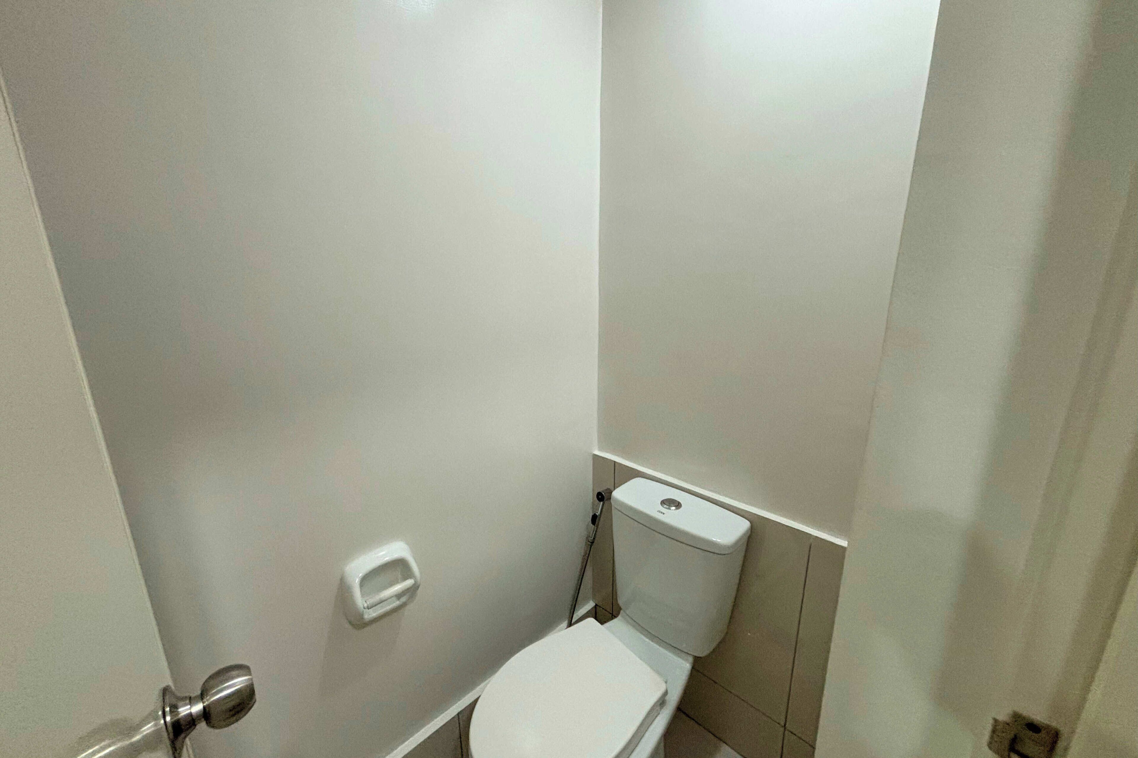 Ein kleines, weißes Badezimmer mit Toilette, einem Händetrockner und einem an der Wand befestigten Seifenspender.