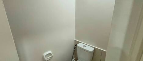 Un baño pequeño y blanco con inodoro, secamanos y dispensador de jabón en la pared.