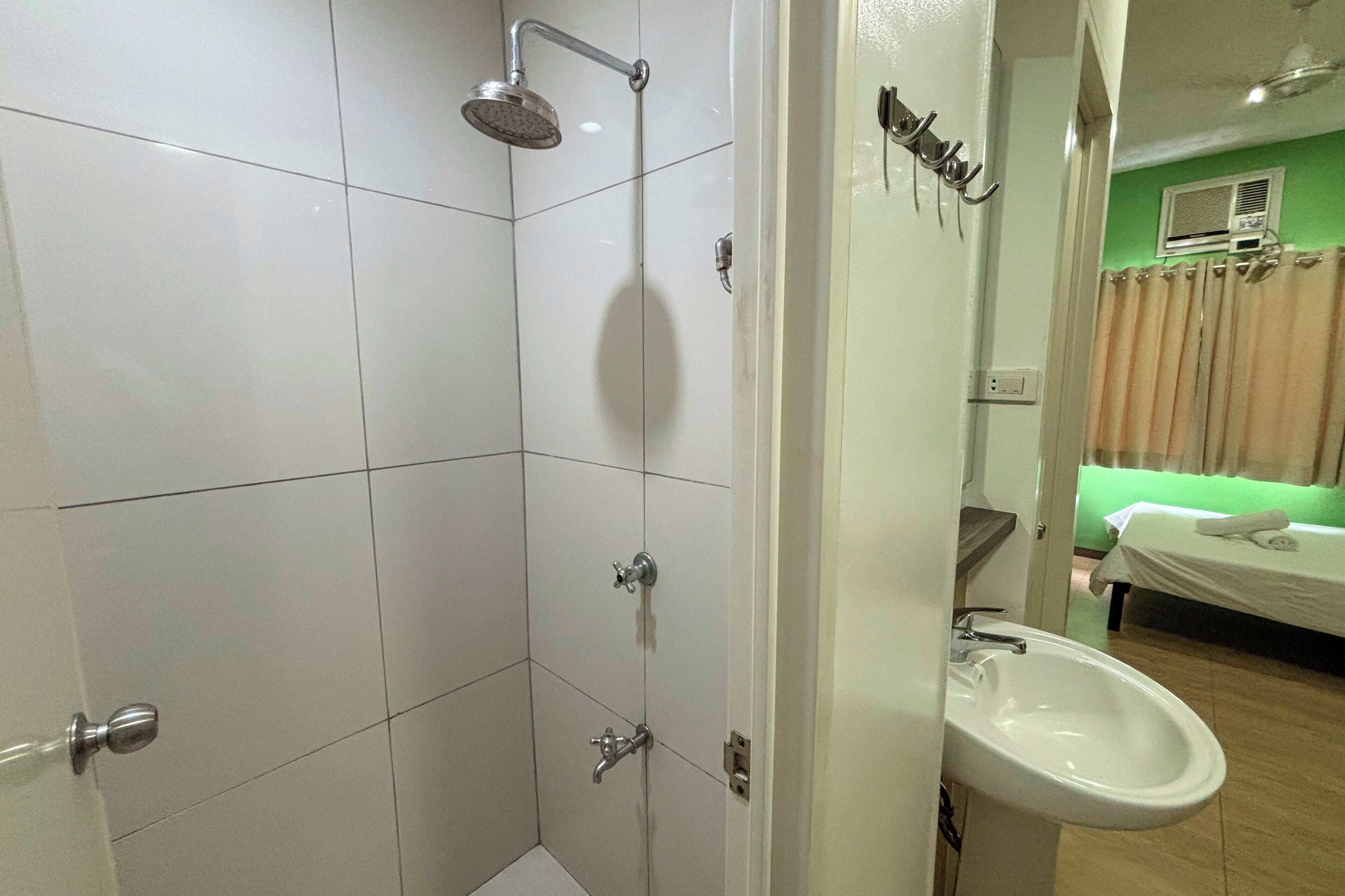 A bathroom with a shower, a sink, and a bed in the adjacent room.