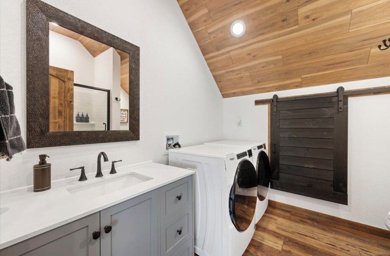 A laundry room with a white sink, a mirror, and a wooden ceiling.