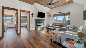 Ein geräumiges Wohnzimmer mit Kamin, Deckenventilator und großen Fenstern mit Blick ins Freie.