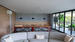 Een moderne woonkamer met een ruime hoekbank, een eethoek met een houten tafel en stoelen, en een grote schuifpui die leidt naar een buitenruimte met planten.