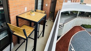 Een balkon met een houten tafel en stoelen, een bakstenen muur en uitzicht op een gebouw met een balkon.