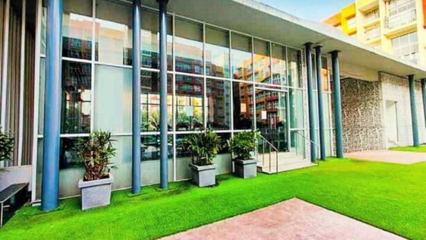 A modern building with large glass windows, a green lawn, and a paved walkway.