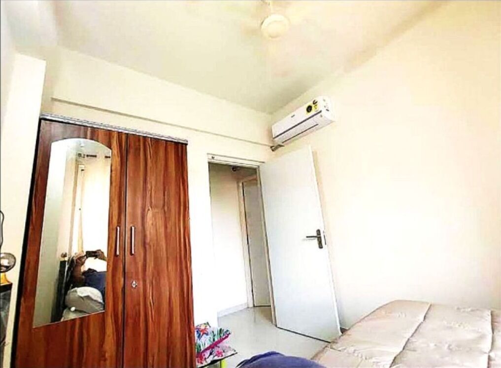 Un dormitorio con un armario de madera, una cama, un equipo de aire acondicionado y una puerta que da a otra habitación.