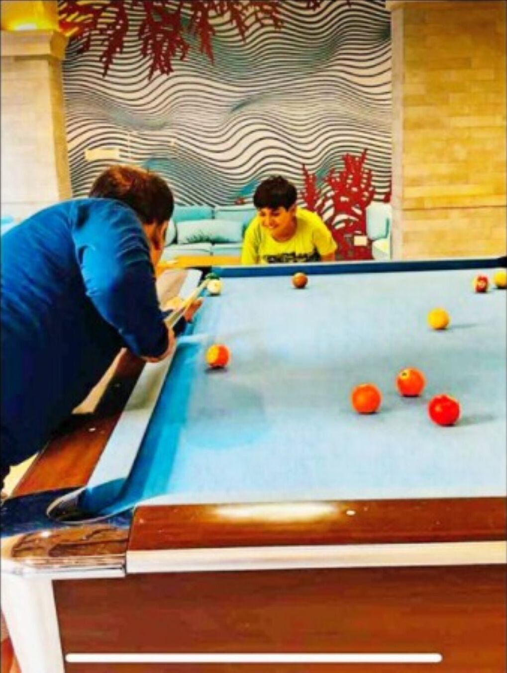 Une table de billard avec des billes et une personne portant une veste bleue, penchée au-dessus.