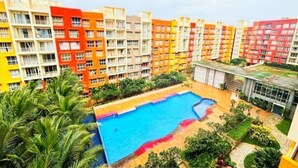 A residential building with multiple colorful apartment units, a swimming pool, and surrounding greenery.