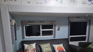 Un espacio de sala acogedor con un sofá de cuero oscuro, dos ventanas y una pared decorativa.