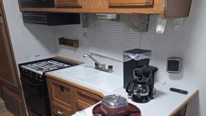 Una cocina compacta con armarios de madera, microondas, estufa, fregadero y cafetera.