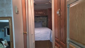 Un pasillo estrecho con una cama al fondo, armarios de madera y un ventanal pequeño.