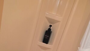Un baño con una bañera color beige, un inodoro blanco y un estante con una botella negra etiquetada como 'BODY WASH'.