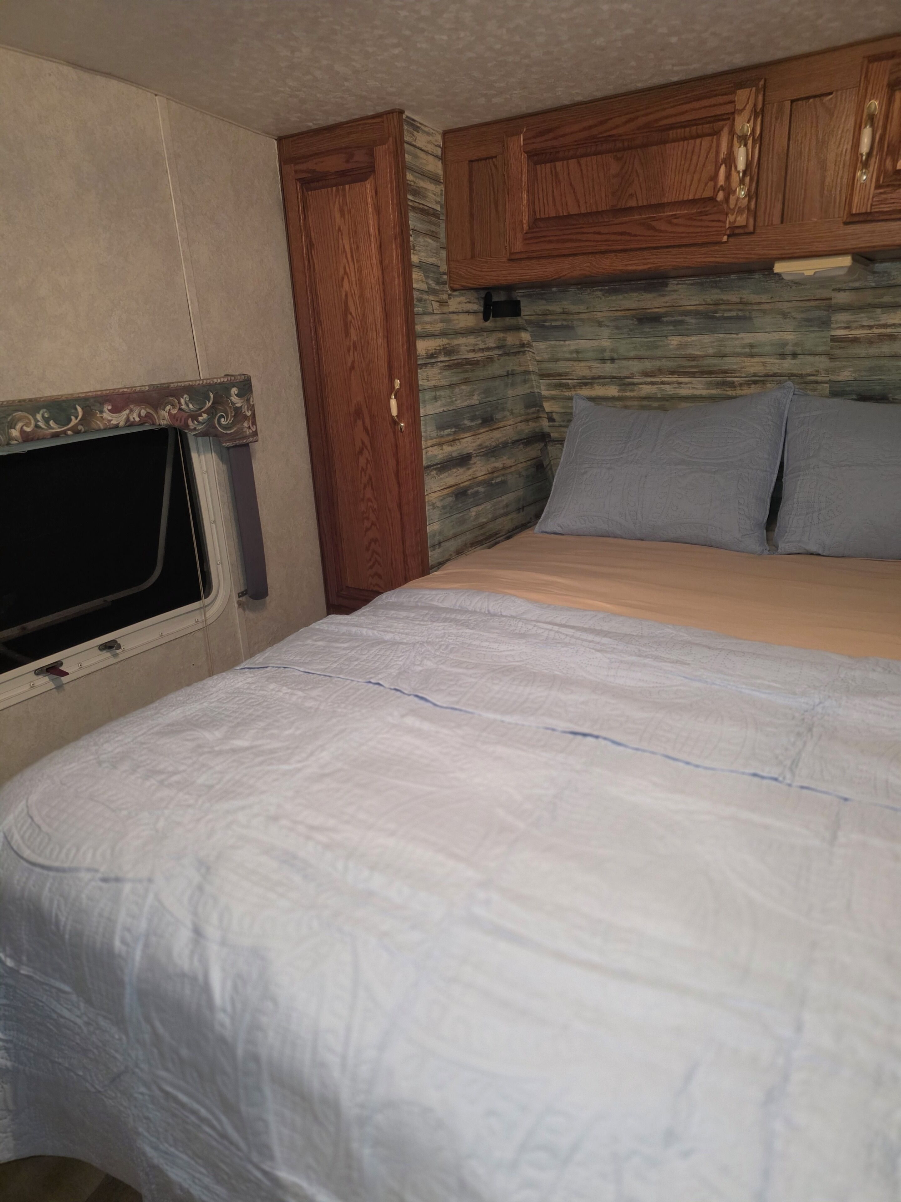 A bedroom with a bed, a window, and wooden cabinets.