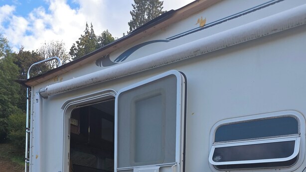 Una caravana blanca con terraza de madera, puerta corredera y ventana.
