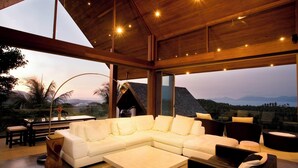 Una sala de estar moderna con un sofá modular grande, una mesa de centro y un comedor con mesa y sillas. La habitación cuenta con ventanas grandes que ofrecen vistas a las montañas.