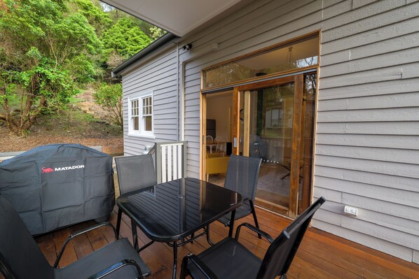 An outdoor patio with a glass door leading to a covered area, a barbecue grill, and a table with chairs. - Ferntree Digs Cottage (Warburton)