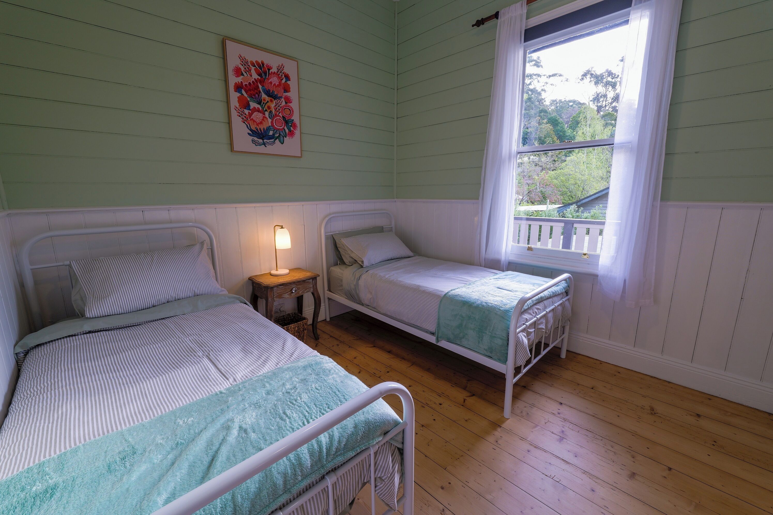 A room with two beds, a window with a view, and a painting on the wall.